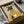 May include: Framed art print of a greyhound wearing a mustard yellow turtleneck sweater, holding a white coffee cup with steam rising. The dog has dark fur and alert ears against a cream background. The print sits in a black frame inside a cardboard shipping box with protective tissue paper, surrounded by wooden frame corners and packaging materials on a table surface.