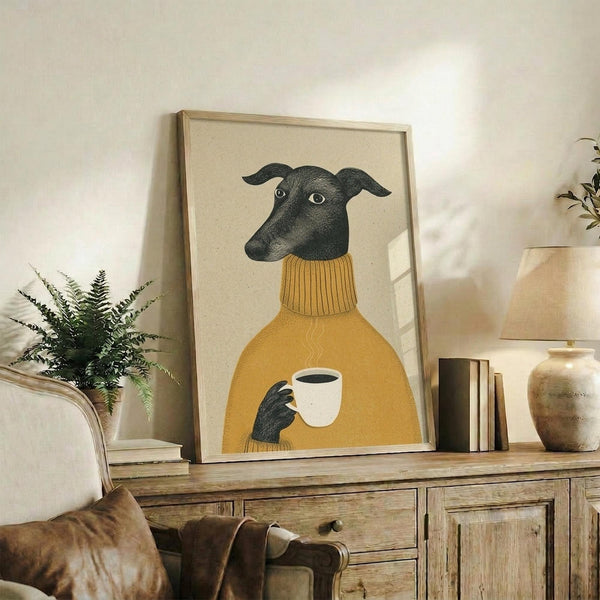 May include: Framed artwork showing a black greyhound wearing a mustard yellow ribbed turtleneck sweater, holding a white coffee cup, displayed on a rustic wooden sideboard alongside books, a small potted fern, ceramic vases, and brown leather furniture in a warm, neutral-toned living room setting.