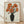 May include: A framed botanical print displayed against a white wall on light wooden flooring. The artwork features orange poppies with black centers arranged in a dark green vase, rendered in vintage Japanese woodblock print style with visible wood grain texture in the background. The piece is housed in a natural wood frame and casts soft shadows on the textured white wall behind it.