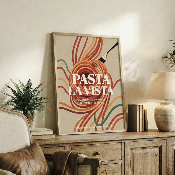 May include: Framed retro-style poster with colorful swirling pasta noodles in red, orange, and green tones against cream background, displaying "PASTA LA VISTA" text with tagline below. Shows wooden sideboard styling with potted fern, ceramic vase, stacked books, and brown leather chair in warm-toned living room setting.