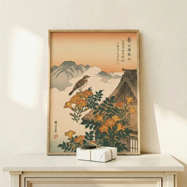 May include: Japanese woodblock print in light wooden frame showing a brown bird perched above orange trumpet vine flowers climbing a traditional thatched roof house, with misty mountains and clouds in background, displayed on cream wooden console table beside small white wrapped gift box against white wall