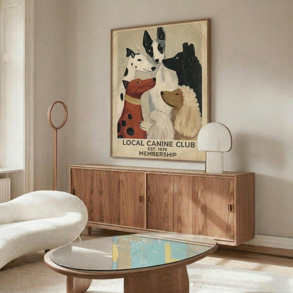 May include: Framed vintage-style poster showing illustrated dogs of various breeds including dalmatian, terrier, and poodle with "Local Canine Club Est. 1976 Membership" text, displayed above mid-century walnut credenza in modern living room with white curved chair, brass floor lamp, and glass coffee table