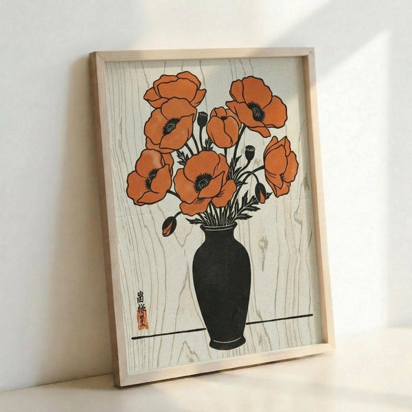 A framed art print featuring orange poppies in a dark green vase against a light wood grain background. The botanical illustration shows several blooming poppies with black centers and unopened buds, rendered in a Japanese woodblock print style. The artwork includes Japanese characters and a red stamp in the lower left corner. The print is displayed in a light wooden frame and photographed leaning against a white wall.