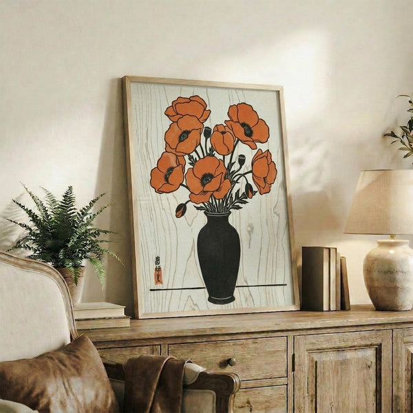 May include: Framed botanical art print featuring orange poppies in black vase on wood grain background, displayed on rustic wooden sideboard alongside fern plant, ceramic vase, and stacked books in neutral-toned living room setting with beige armchair and soft natural lighting.