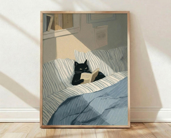 May include: Framed poster print showing a black cat with yellow eyes reading an open book while sitting on striped bedding. The illustration features muted blue and beige tones with sunlight streaming across the bed. Bookshelves are visible in the background. The artwork is displayed in a light wood frame, leaning against a white wall on wooden flooring.