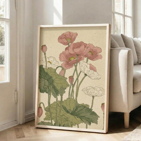 May include: Large framed botanical print leaning against white wall showing pink and white poppies with green leaves in vintage illustration style. Cream-colored artwork in light wood frame positioned next to beige upholstered chair near bright windows in modern living room setting.