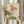May include: Person in cream ruffled sleeves holding framed botanical illustration of pink and white poppies with green leaves against beige background. Dried pampas grass visible to left. Natural lighting from window creates soft shadows on neutral wall.