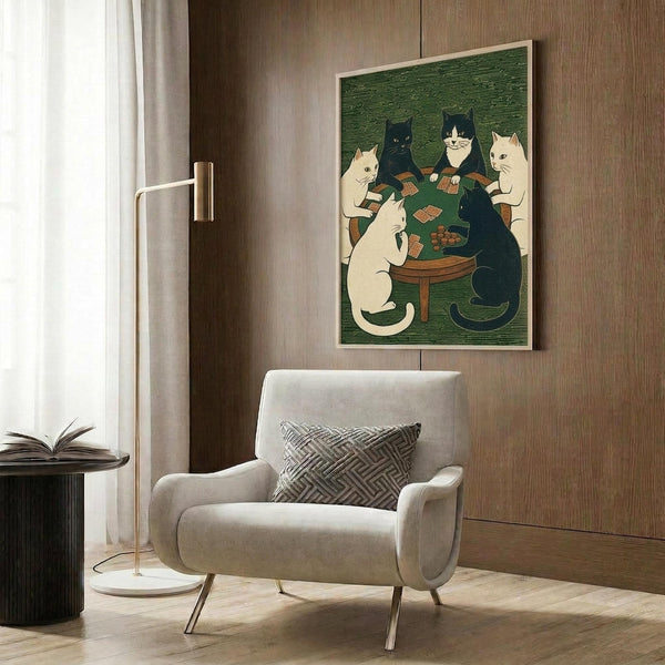 May include: Framed poster featuring cats playing cards around a green table in woodblock print style, displayed on wood paneled wall above beige upholstered chair with geometric pillow. Room shows modern brass floor lamp, dark side table with open book, and neutral decor with natural lighting from window.