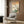 May include: Japanese woodblock print artwork hanging on wood-paneled wall above cream upholstered armchair with geometric pillow. Print features Mount Fuji in background with pink cherry blossoms, blue bird perched on branch, and Japanese calligraphy on cream background with light wood frame. Modern floor lamp and side table with open book complete the neutral-toned reading nook scene.