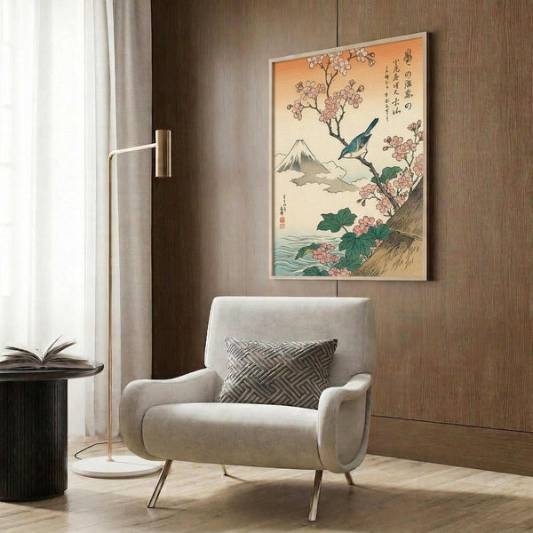 May include: Japanese woodblock print artwork hanging on wood-paneled wall above cream upholstered armchair with geometric pillow. Print features Mount Fuji in background with pink cherry blossoms, blue bird perched on branch, and Japanese calligraphy on cream background with light wood frame. Modern floor lamp and side table with open book complete the neutral-toned reading nook scene.