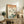 May include: Vintage Japanese woodblock print featuring Mount Fuji in background with cherry blossom tree, blue bird perched on branch, and flowing water below. Print displayed in light wooden frame on rustic wood sideboard alongside woven basket with fern plant, ceramic vase, and books. Warm neutral room setting with cream chair visible.