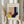 May include: Person holding framed Bauhaus-style geometric art print with abstract shapes in mustard yellow, coral pink, navy blue, and light blue colors. Dried pampas grass visible on left side. Light wooden frame against neutral beige background with soft natural lighting.