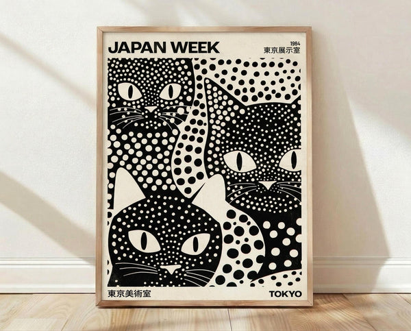 May include: Black and white poster print featuring stylized cat faces with polka dot patterns in a wooden frame, leaning against white wall on light wood flooring. The artwork shows three cat faces with distinctive eyes and whiskers created using various sized dots and circles in a bold graphic style.