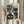 May include: Person in cream sweater holding framed black and white polka dot poster featuring stylized cat faces with whiskers and geometric patterns. Light wood frame against neutral curtained background with dried wheat stems visible on left side.