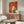 May include: Colorful abstract dog illustration artwork displayed above a walnut credenza in a modern living room. The painting features four stylized dog faces in warm oranges, reds, yellows, blues and greens against a vibrant geometric background. Room shows white curved chair, glass-top oval coffee table, white mushroom lamp, and brass floor lamp on light hardwood floors.