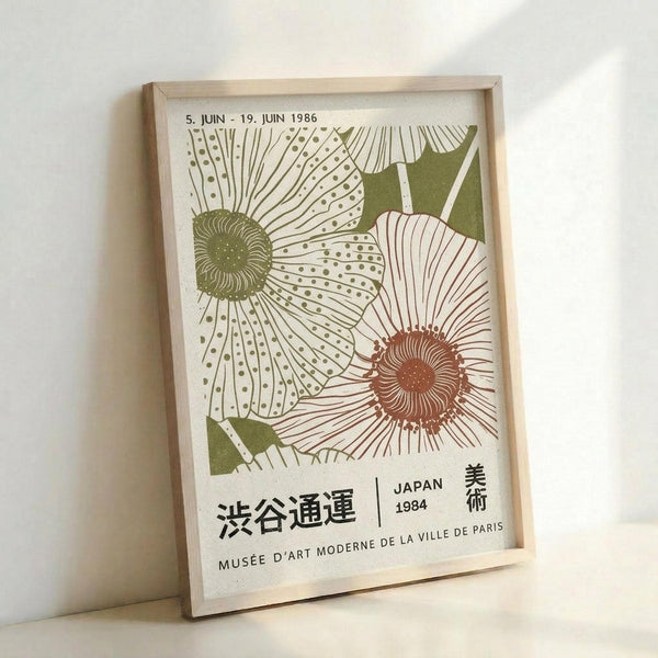 May include: Framed vintage-style exhibition poster featuring two large stylized flowers with detailed line work and dotted patterns. One flower has a green center with white petals, the other has a terracotta-colored center. Green leaves accent the design. Japanese text and "MUSÉE D'ART MODERNE DE LA VILLE DE PARIS" appear at bottom with dates "5. JUIN - 19. JUIN 1986" and "JAPAN 1984". Light wooden frame sits against white wall with soft shadow.