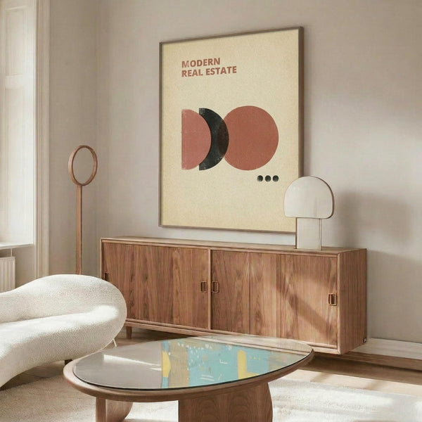 May include: Modern minimalist poster with geometric shapes in terracotta, pink, and dark green on cream background, displayed in thin frame above walnut credenza. Room features white curved chair, oval glass coffee table with colorful abstract surface, copper floor lamp, and white table lamp. Soft natural lighting creates warm shadows on neutral walls.
