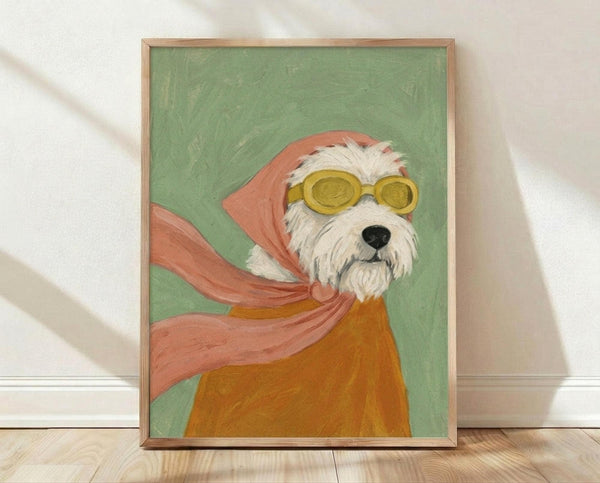 May include: Framed artwork leaning against white wall on light wooden floor. The painting shows a white fluffy terrier dog wearing yellow goggles, coral pink hood and flowing scarf against sage green background. Artwork has natural wood frame and painterly brushstroke texture. Soft natural lighting creates gentle shadows on the white textured wall behind.