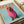 May include: Fashion magazine cover poster featuring a brown dachshund wearing an oversized pink knit turtleneck sweater against a light blue background. The dog's head pokes through the collar opening with an endearing expression. Red "DOGUE" text appears at the top in bold serif letters mimicking luxury fashion magazine typography. Print sits on white bedding next to cream ribbon, showing the artwork's scale and home decor styling potential.