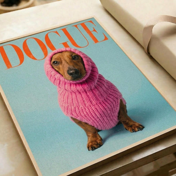 May include: Fashion magazine cover poster featuring a brown dachshund wearing an oversized pink knit turtleneck sweater against a light blue background. The dog's head pokes through the collar opening with an endearing expression. Red "DOGUE" text appears at the top in bold serif letters mimicking luxury fashion magazine typography. Print sits on white bedding next to cream ribbon, showing the artwork's scale and home decor styling potential.