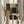 May include: Person in beige ruffled sleeves holding framed abstract geometric artwork featuring overlapping rectangular and rounded shapes in muted tones of sage green, dusty blue, coral pink, cream, and black with visible brushstroke texture. Dried pampas grass visible to left against soft natural lighting and neutral curtained background.