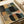 May include: Abstract geometric poster print displayed on white paper with cream-colored tube nearby. Artwork features overlapping rounded rectangular shapes in black, coral pink, sage green, dusty blue, and cream arranged in a grid-like composition with visible brush texture and muted earth tones.