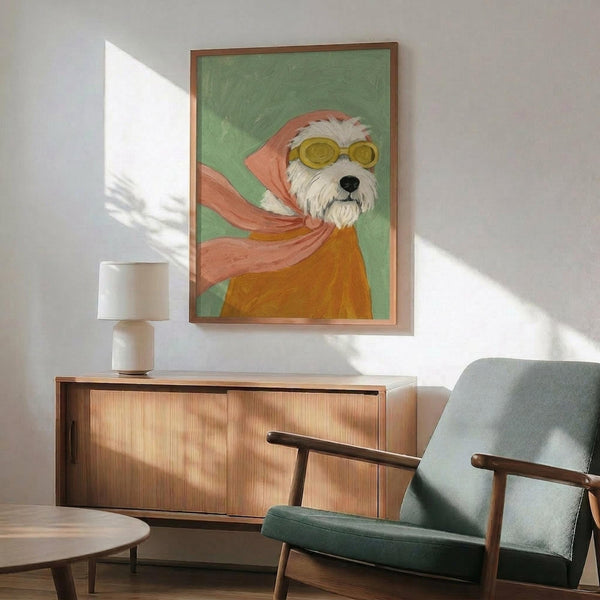 May include: Framed artwork showing a white terrier dog wearing yellow goggles and a flowing pink-orange scarf against a sage green background, displayed above a mid-century modern wooden credenza with table lamp, next to a mint green upholstered armchair in a sunlit room with white walls.