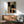 May include: Abstract geometric artwork with overlapping colorful rectangles and black rounded shapes in wooden frame, displayed above mid-century modern walnut credenza with table lamp, next to sage green upholstered armchair with wood arms in sunlit room with white walls