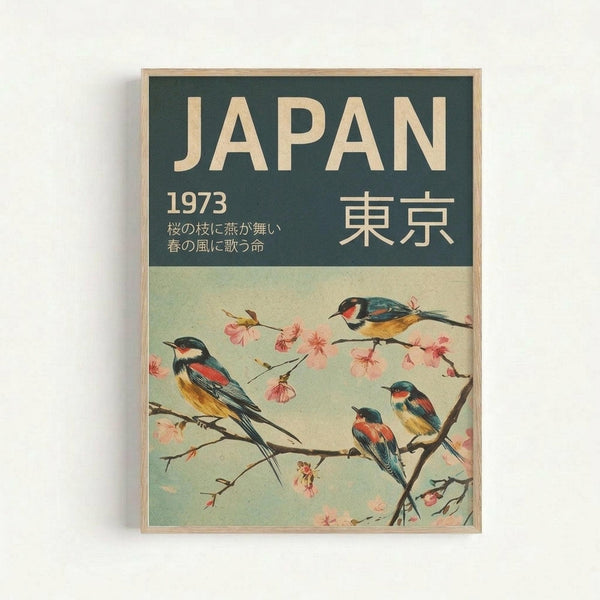 Vintage-style travel poster featuring four colorful birds perched on cherry blossom branches against a pale green background. The poster has a dark teal header with "JAPAN" in cream letters, "1973" and Japanese characters, plus Japanese text below. The birds display blue, red, yellow and black plumage among delicate pink sakura flowers. Displayed in a light wood frame against a white wall.