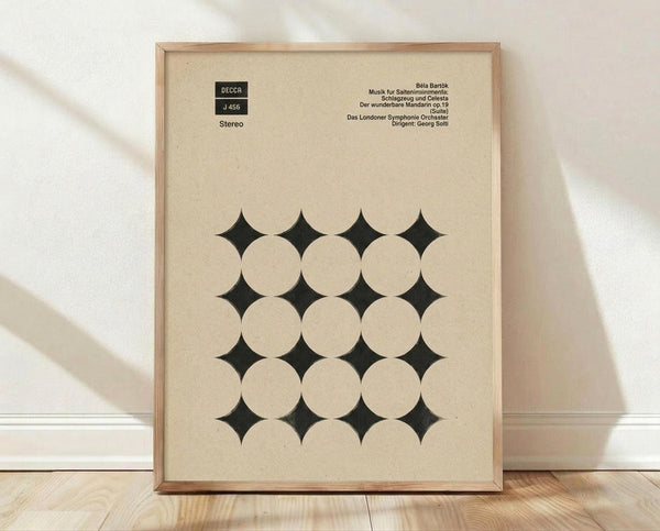 May include: Framed vintage album cover poster with cream background featuring geometric pattern of white circles and black diamond shapes in grid formation. Text shows Decca record label, stereo designation, and German text for Béla Bartók classical music. Natural wood frame displayed on light wooden floor against white wall with soft shadows.