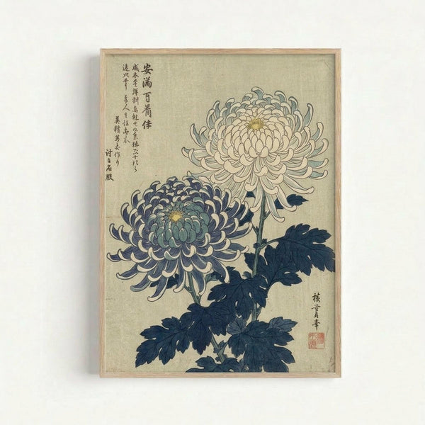 Vintage Japanese botanical illustration featuring two chrysanthemum flowers in cream and blue-purple tones with dark navy leaves, displayed in a light wood frame against a white wall. The artwork shows delicate layered petals with yellow centers and includes traditional Japanese calligraphy text on the left side and a red artist seal on the right.