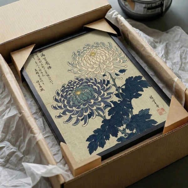 May include: Japanese woodblock print artwork in black frame showing two chrysanthemum flowers - one cream colored, one blue-green - with dark blue leaves and Japanese text. Print is packaged in cardboard box with tissue paper and wooden dowels, photographed on white fabric surface next to dark glass object.