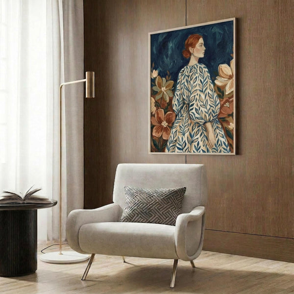 May include: Portrait artwork of a red-haired woman in profile wearing a blue and white patterned dress, surrounded by large brown and orange flowers against a dark blue background. The framed print hangs on wood-paneled walls above a cream upholstered armchair with geometric pillow. Modern brass floor lamp and round side table with open book complete the styled living room scene.