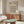 May include: Framed geometric poster with cream background featuring black circles and diamond pattern, displayed above wooden credenza in minimalist living room with white curved chair, brass floor lamp, glass coffee table, and white table lamp