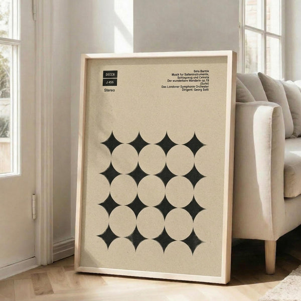 May include: Framed vintage album cover poster with geometric pattern of cream circles creating dark diamond shapes between them, displayed in light wooden frame leaning against beige chair in bright room with white walls and windows, natural lighting casting shadows on hardwood floor.