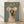 May include: Framed poster print featuring an Italian Greyhound wearing a cream knitted sweater with colorful pom-pom ear warmers against a sage green background. Gold "DOGUE" text appears at top in fashion magazine style. Natural wood frame sits on light wooden floor against white wall with soft shadows.