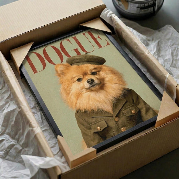 May include: Framed poster print featuring a fluffy orange Pomeranian dog wearing a military-style olive green uniform and cap, styled like a vintage fashion magazine cover with "DOGUE" in red letters. The black-framed artwork sits in an open cardboard shipping box with white tissue paper, surrounded by brown paper wrapping materials on a white surface.