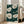May include: Framed botanical art print leaning against white wall next to beige upholstered chair in bright living room. The artwork features large white poppy flowers with detailed centers on deep emerald green background with white dots, displayed in light wood frame on hardwood floor near tall windows.