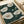 May include: Vintage botanical art print featuring white poppies with detailed line work on dark green background with white dots, displayed in light wood frame on white bedding next to cream ribbon, showing elegant floral illustration in muted earth tones with intricate petal texturing and long stems.