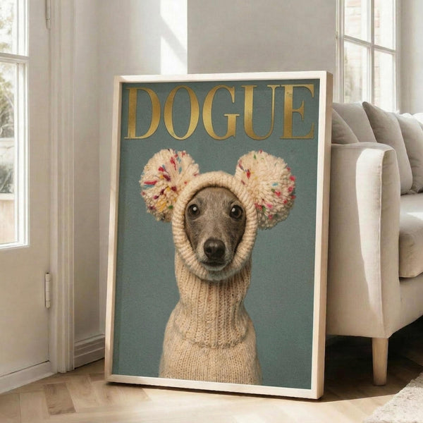 May include: Framed poster artwork featuring a greyhound wearing a cream knitted sweater with colorful pom-pom ear warmers against a teal background, with gold "DOGUE" text at top. Light wood frame leans against white wall next to beige upholstered chair in bright room with large windows and hardwood floors.