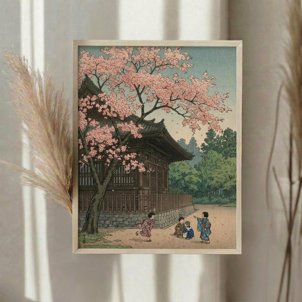 May include: Framed Japanese woodblock print showing cherry blossoms over traditional temple building with small figures below, displayed on white wall next to dried wheat stalks. Print features soft pink blossoms, green foliage, and muted earth tones in classic ukiyo-e style with thin light wood frame.