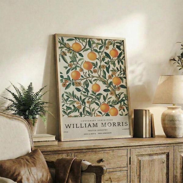 May include: Framed botanical poster featuring orange fruit and green foliage pattern displayed on rustic wooden sideboard beside fern plant, books, and ceramic vases in warm-toned living room setting with beige armchair and white walls