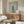 May include: Framed poster featuring a cream-colored poodle wearing a teal turtleneck sweater and matching boots against a light blue background with "DOGUE" text in gold letters, displayed above a walnut credenza in a modern living room with white curved chair, glass coffee table, and white table lamp