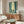 May include: framed poster showing two samurai warriors dueling with swords in a misty bamboo forest, displayed above a wooden sideboard in a minimalist living room with cream walls, white curved chair, glass coffee table, and modern lighting fixtures