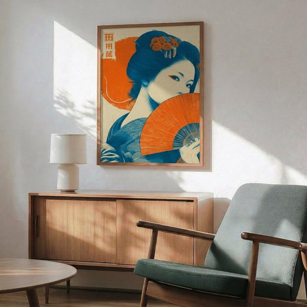 May include: Japanese-style artwork showing a geisha with blue-black hair adorned with orange flowers, holding a vibrant orange fan against an orange background. The poster features Japanese characters in the upper left corner and displays a traditional ukiyo-e art style with bold blues and oranges. Shown framed in light wood hanging above a mid-century modern wooden sideboard with a ceramic table lamp, next to a sage green upholstered armchair in a bright, minimalist living room with white wall