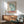 May include: Framed vintage-style poster with blue butterfly wing design and red "TOKYO" text, displayed above wooden sideboard with white table lamp in mid-century modern living room setting with mint green armchair and natural lighting casting shadows on white wall.