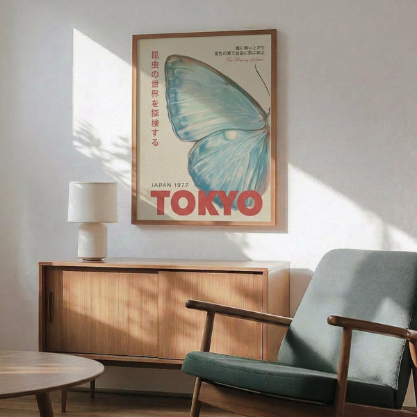 May include: Framed vintage-style poster with blue butterfly wing design and red "TOKYO" text, displayed above wooden sideboard with white table lamp in mid-century modern living room setting with mint green armchair and natural lighting casting shadows on white wall.