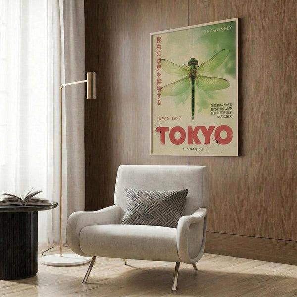 May include: Vintage-style poster featuring green dragonfly with Japanese text and red "TOKYO" lettering, displayed in light wood frame on textured wood paneled wall above cream upholstered armchair with geometric patterned pillow, brass floor lamp and small round table with open book nearby