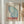 May include: Framed vintage-style poster with blue-green butterfly wing design and Japanese text, mounted on white wall next to dried pampas grass stems. Features "TOKYO" in bold red letters with "JAPAN 1977" above, delicate wing illustration in soft blue and teal watercolor style, housed in light wood frame.