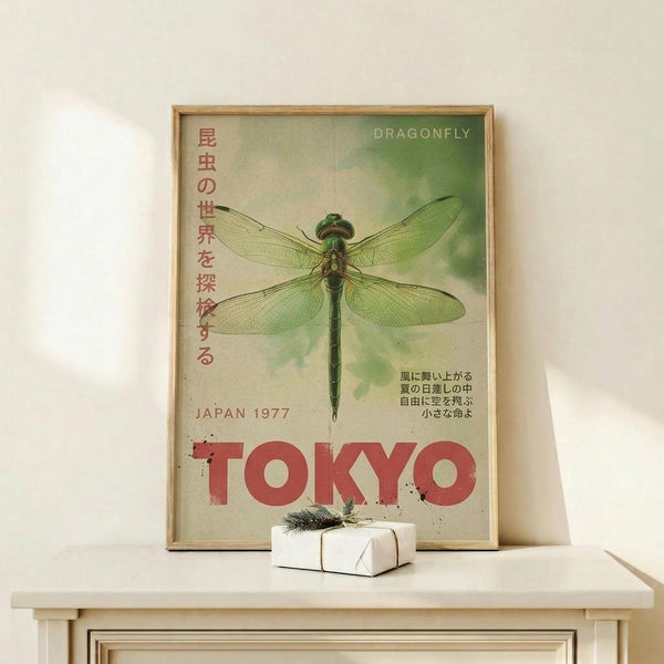 May include: Vintage-style poster featuring large green dragonfly with transparent wings against soft green cloudy background, Japanese text on left side, red "TOKYO" lettering at bottom, "JAPAN 1977" and "DRAGONFLY" text, displayed in thin wooden frame on light wood floating shelf with small white wrapped gift box beside it, against cream colored wall